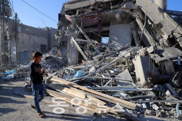 가자지구 남부 도시 칸 유니스에서 한 남자아이가 지난 17일 이스라엘의 습격을 받은 건물 잔해 옆을 지나고 있다.